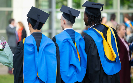 UCD graduates in academic gowns and hoods standing together.